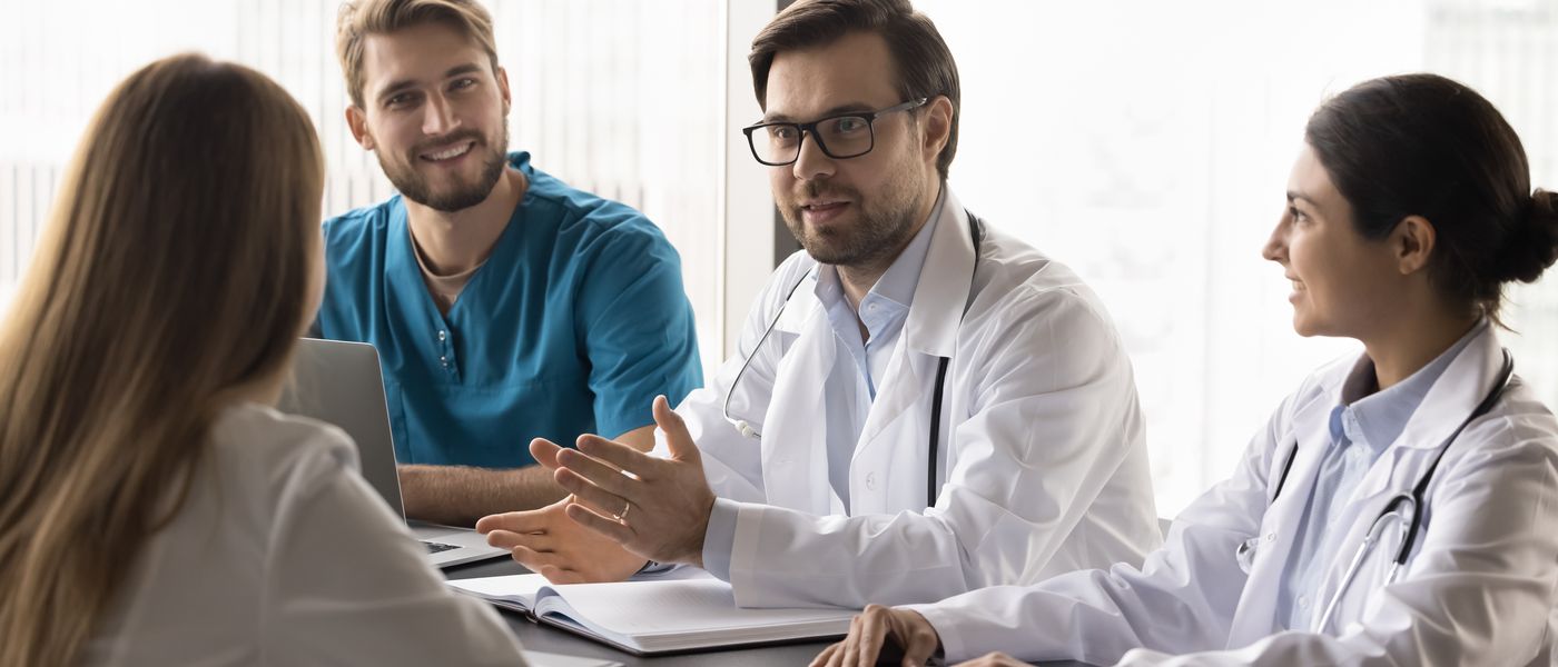 A physician leading a care team discussion at a clinic conference table